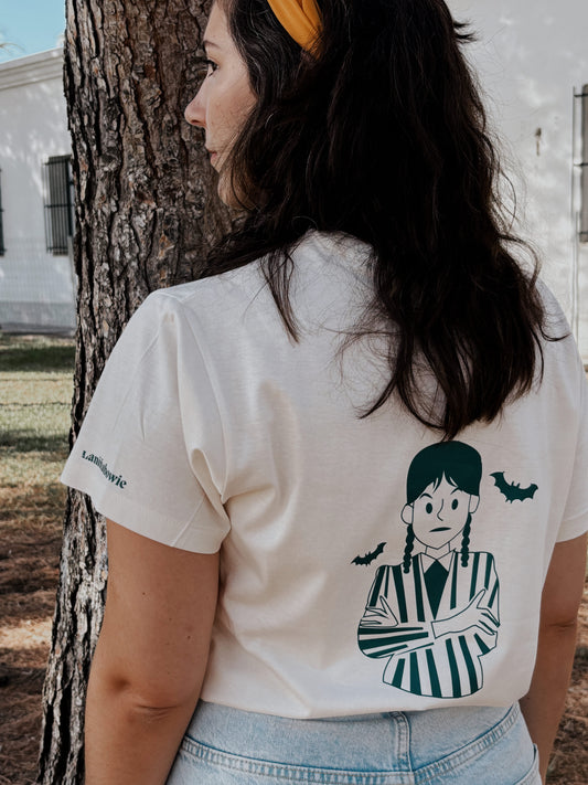 camiseta con diseño de miércoles Addams de Laniñabowie con textura suave. Es de color blanco crea y de algodón orgánico en tallas unisex de la XS a la 3xl.