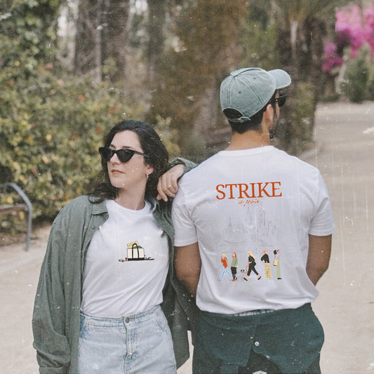 Camiseta de algodón orgánico de Laniñabowie modelo Carolyn en color blanco, con ilustración pequeña en el pecho con detalles como la revista vogue y estampado grande en la espalda con silueta de Nueva York, la frase "STRIKE A POSE" y mujeres caminando con referencia a Carolyn Bessette-Kennedy.